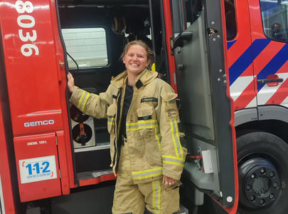 Brandweervrijwilliger Eline bij de deur van een brandweerwagen