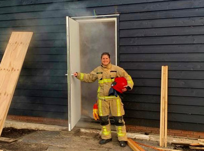 Brandweervrijwilliger Anita in een deuropening van een huis waar rook uitkomt