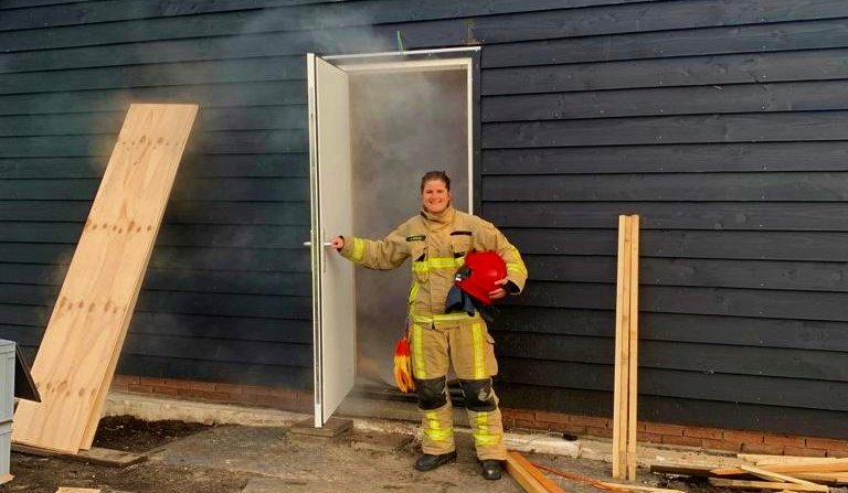 Brandweervrijwilliger Anita in een deuropening van een huis waar rook uitkomt